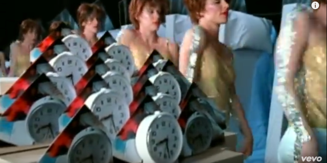 Screenshot of the dissolve between the alarm clocks in the heroine's bedroom to the multiple versions of the heroine-turned-gold lamé disco dancer from the video, "Let Forever Be."