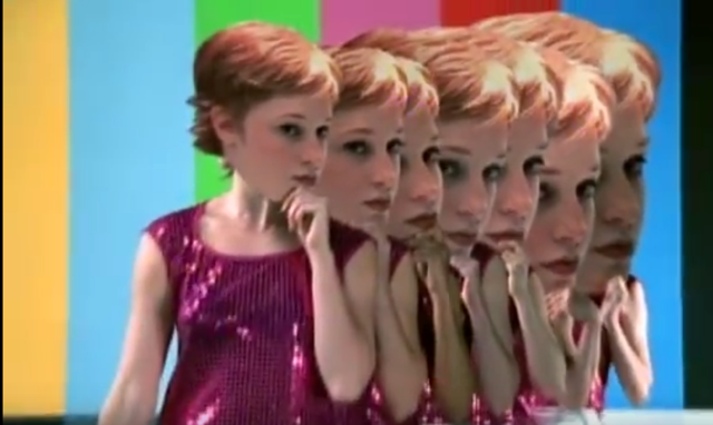 Screenshot of the disco dancers holding oversized cut-outs of the heroine's head over their own faces from the video "Let Forever Be."